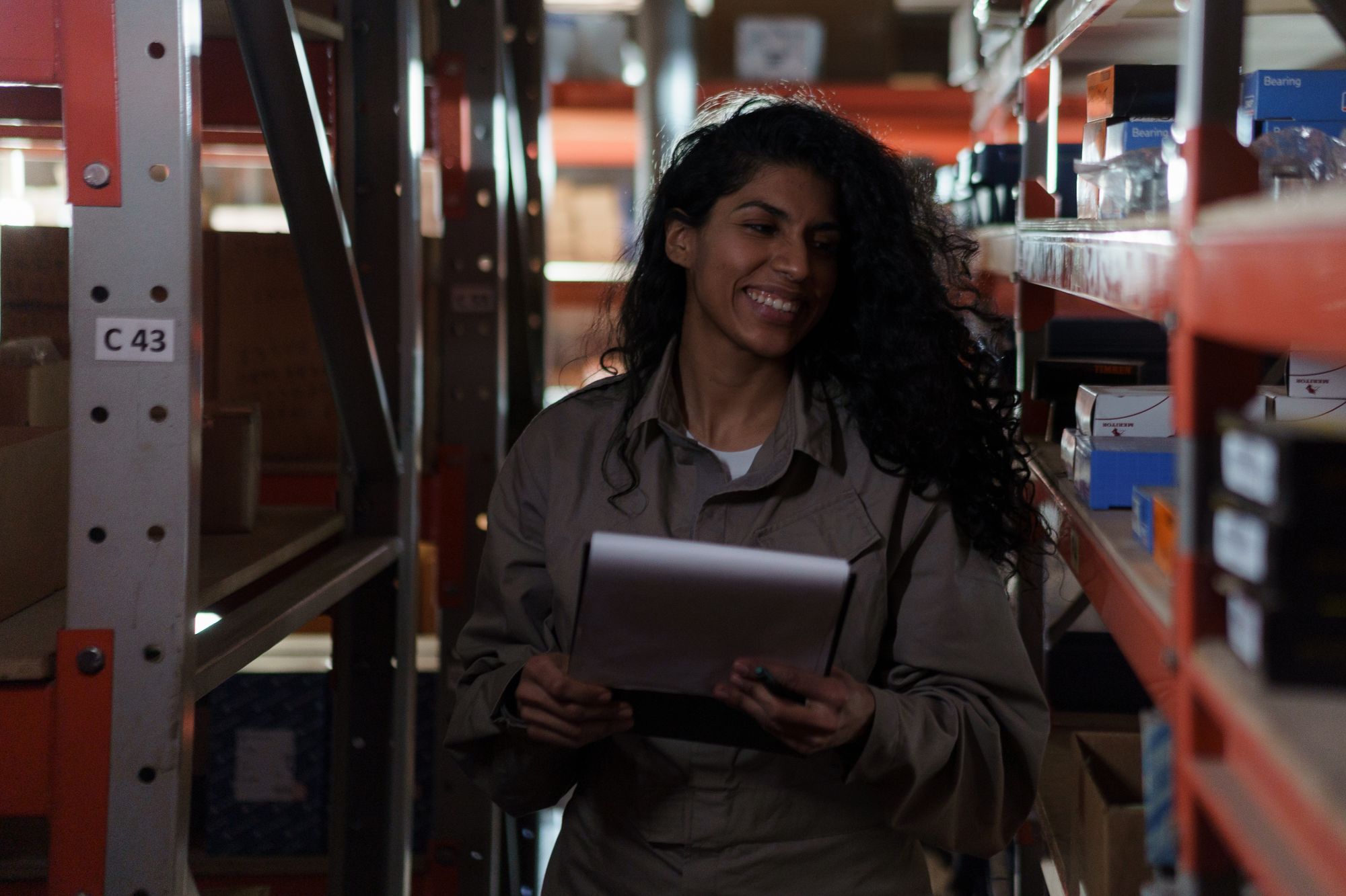 Stockroom worker checking records beside shelves of boxed bearings