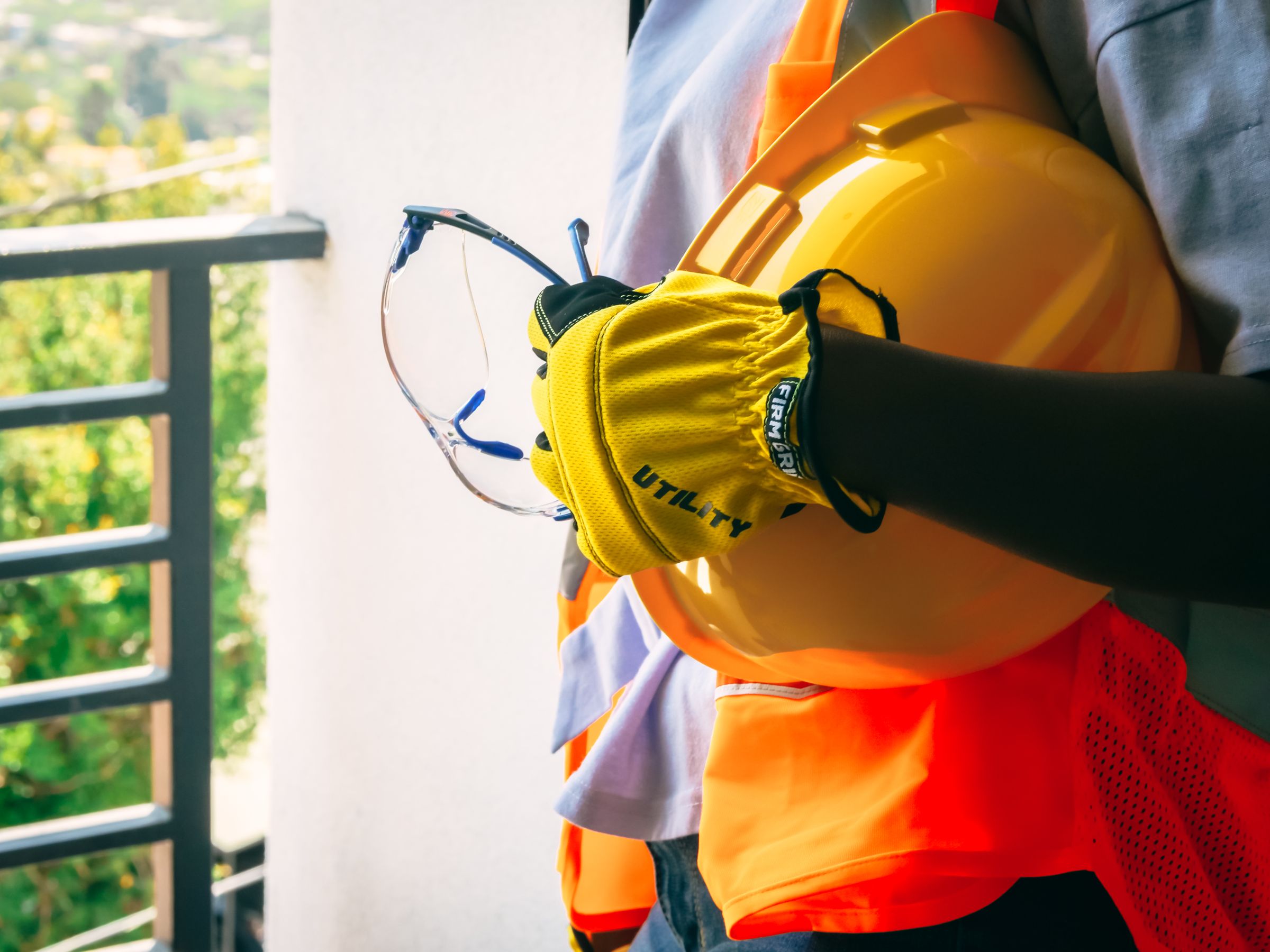Worker holding a hard hat and safety glasses while wearing protective gloves