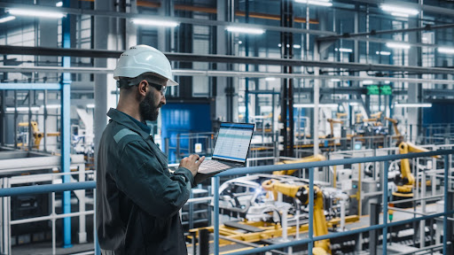 An engineer using a laptop beside factory equipment